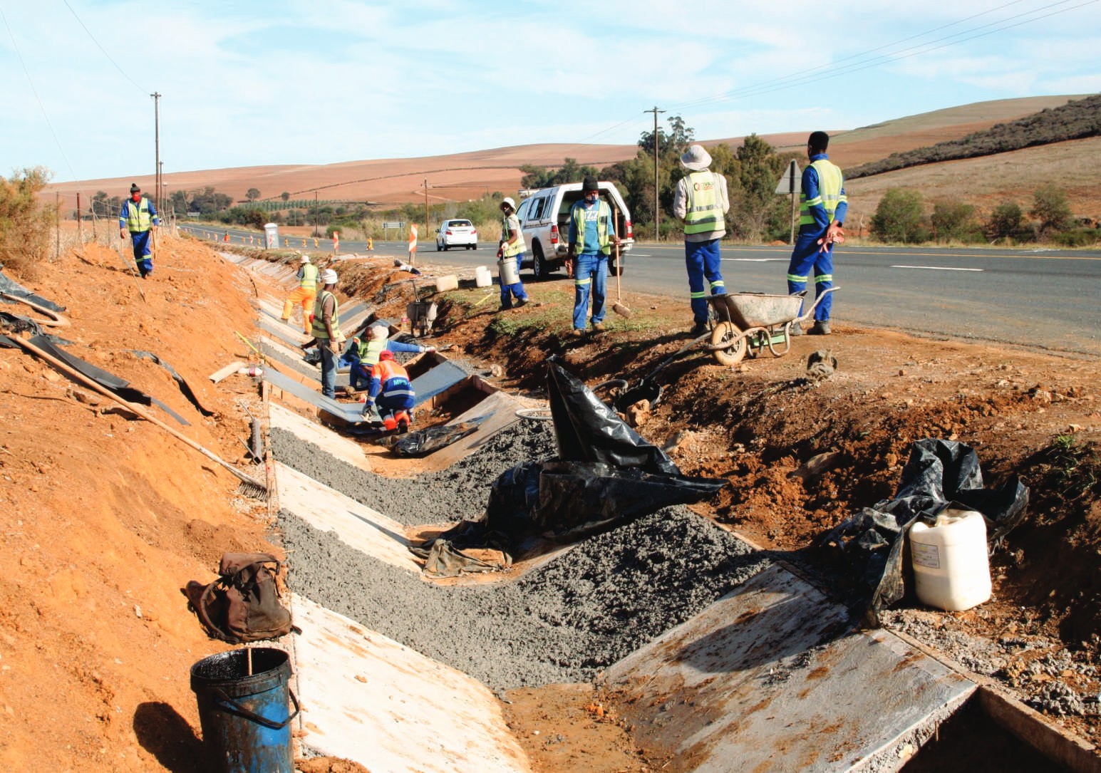 Workers in hi-vis laying a concrete stormwater channel beside a road